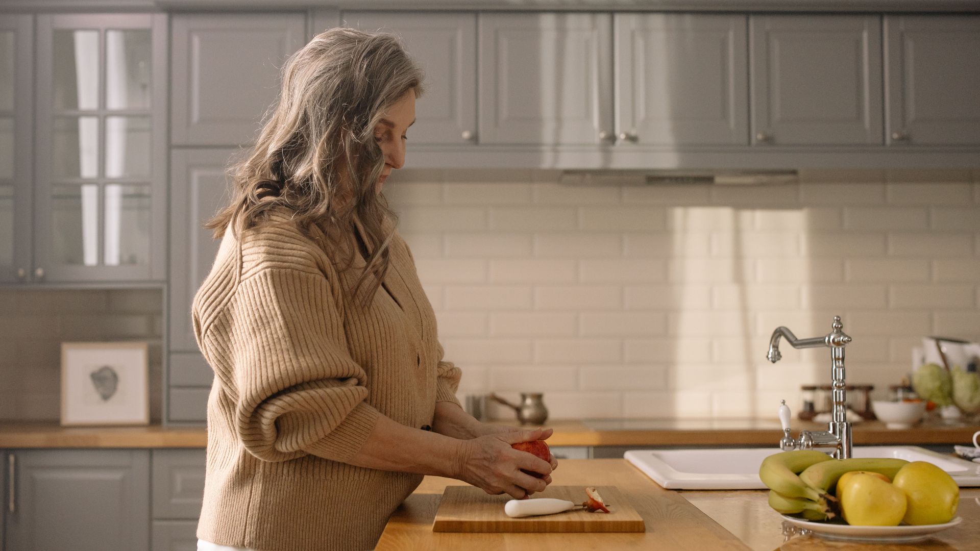 Senior woman slicing fruit in a warm kitchen setting, showcasing home cooking.