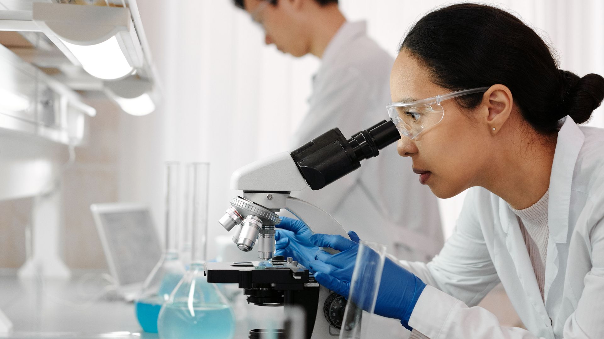 Researchers in a lab analyzing samples using microscopes and glassware.