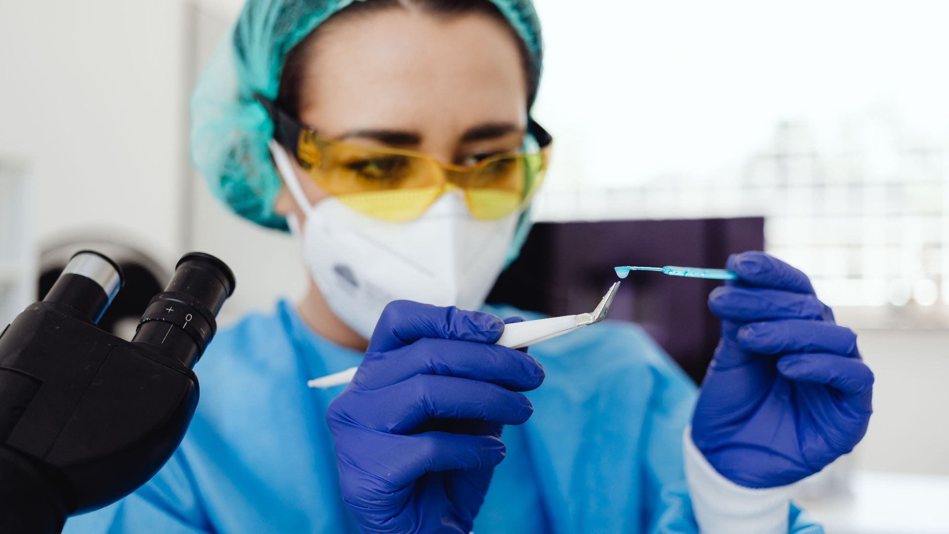 Female scientist in protective gear examines sample indoors, utilizing laboratory equipment.