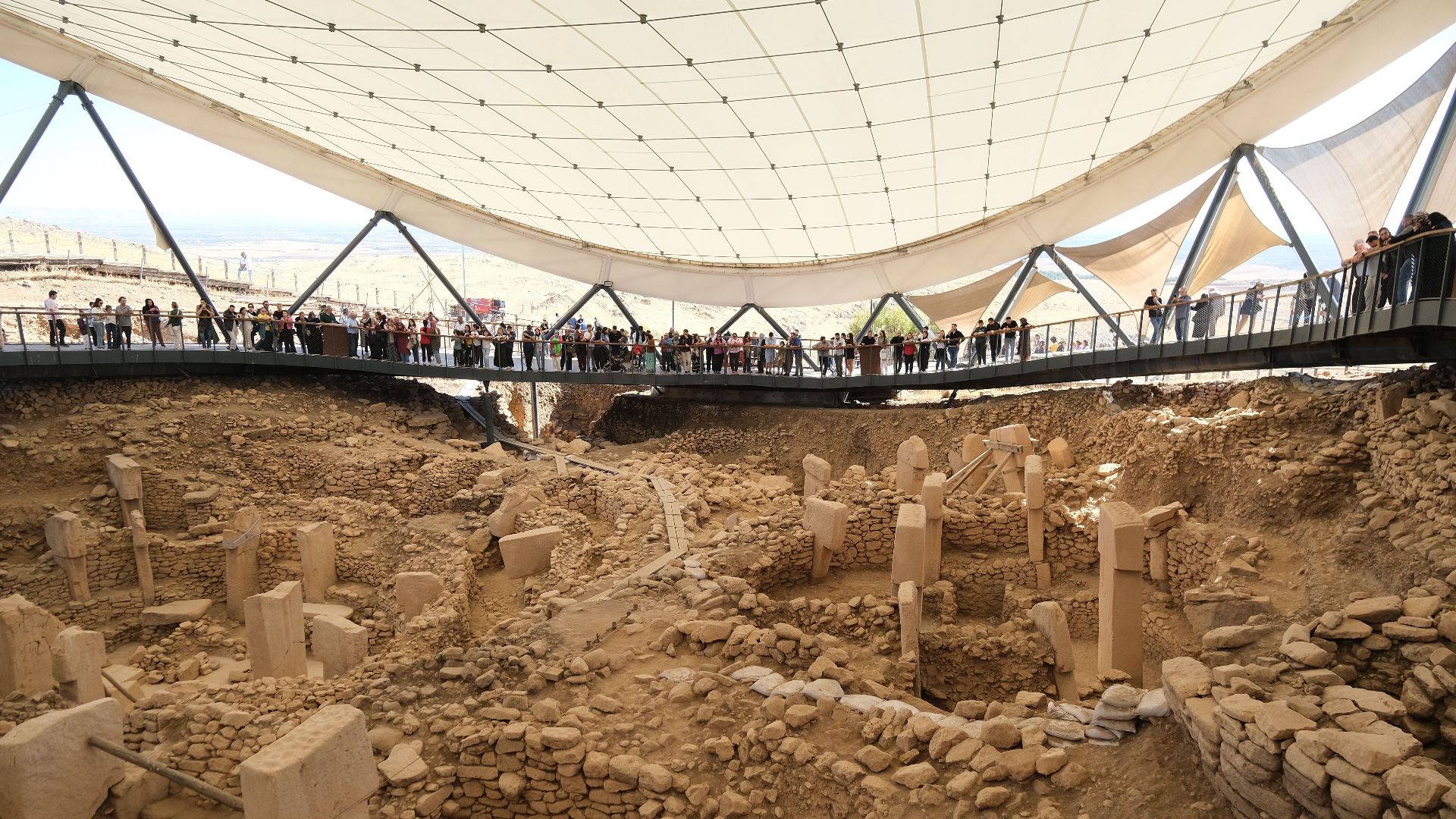 Tourists observing the ancient stone structures of Göbekli Tepe, Turkey, under a modern canopy.