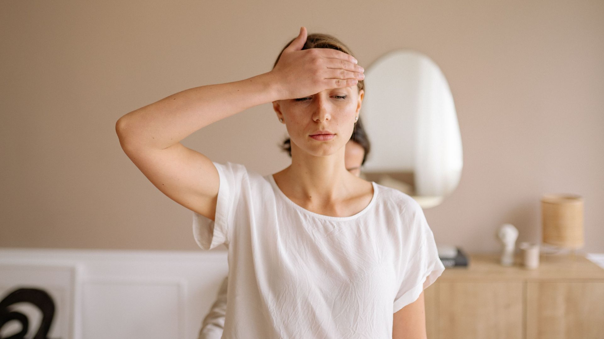 Woman practicing mindfulness meditation with hand on forehead indoors.