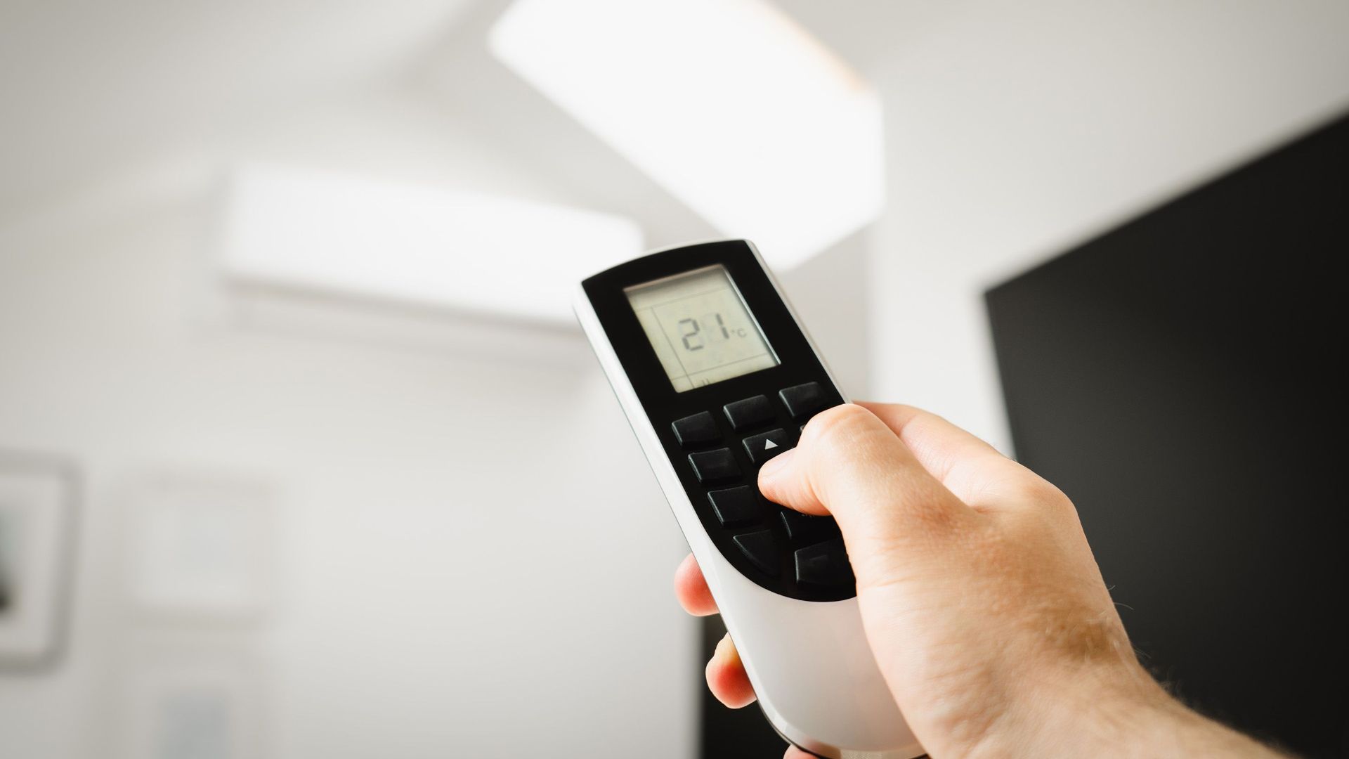 Close-up of a man using a remote to control air conditioning indoors.
