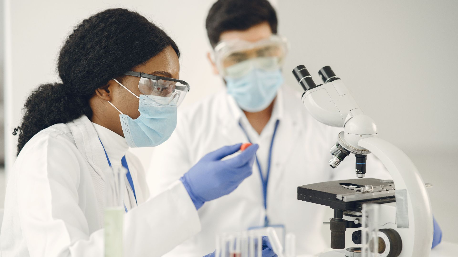 Researchers in protective gear conduct scientific experiments using microscopes in a lab.