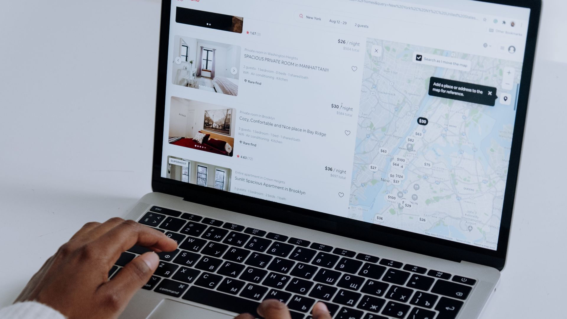 Hands typing on laptop searching Airbnb for accommodation options with map view.