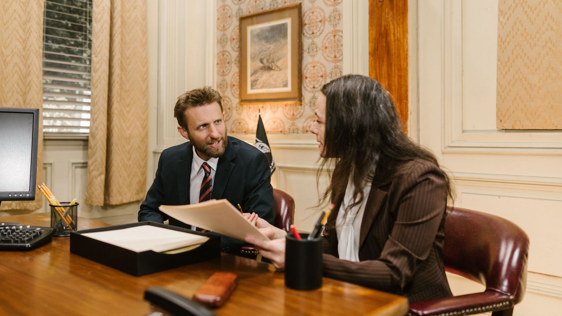 Two professionals engaged in a business discussion in an office setting, reviewing legal documents.