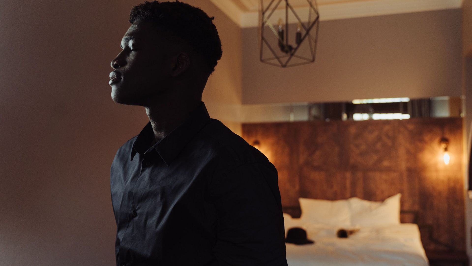 A man stands in a stylish bedroom, exuding calm and introspection.
