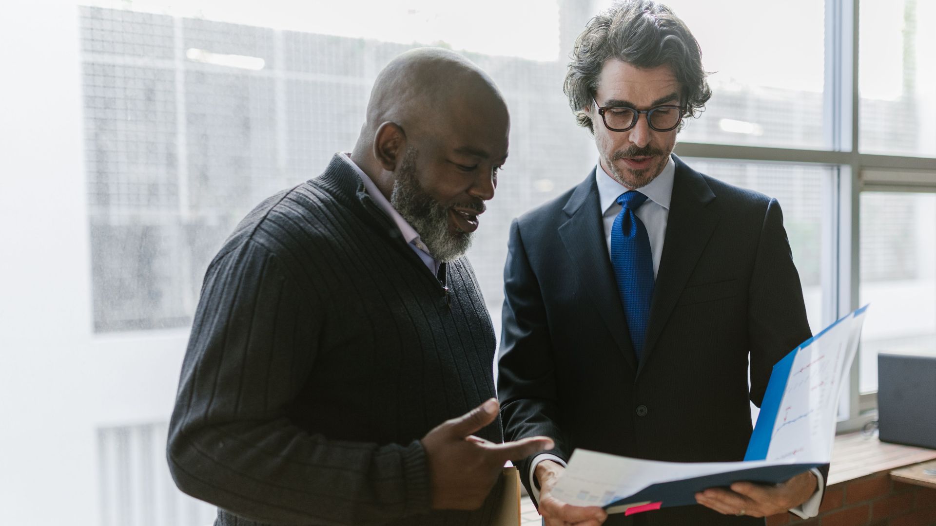 Two businessmen discussing and reviewing documents in a modern office setting.
