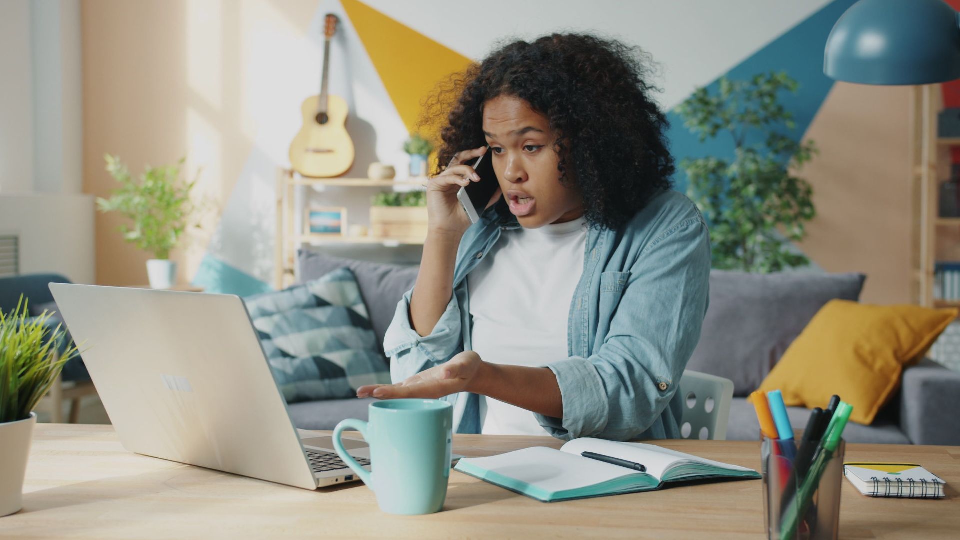 Young woman multitasking in home office environment using laptop and phone.