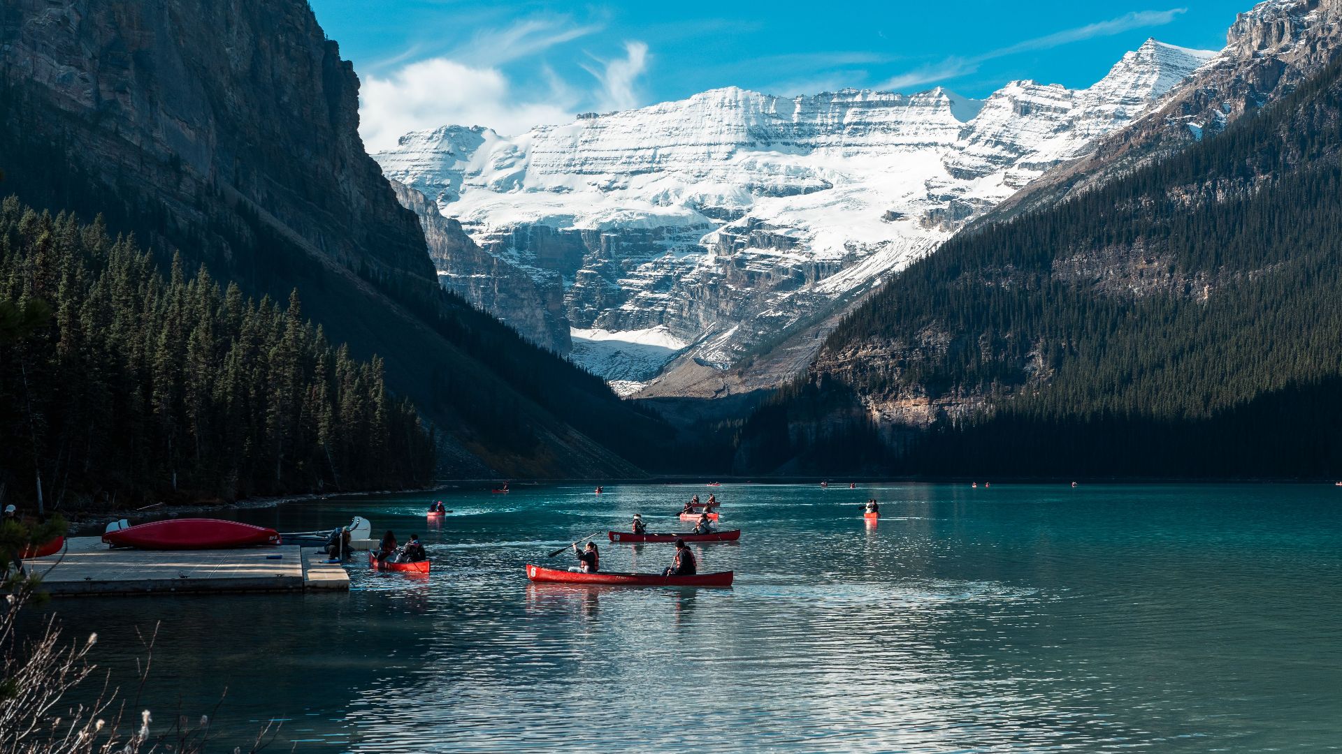 Serene view of canoes on Lake Louise surrounded by snow-capped mountains in Banff National Park, Alberta.