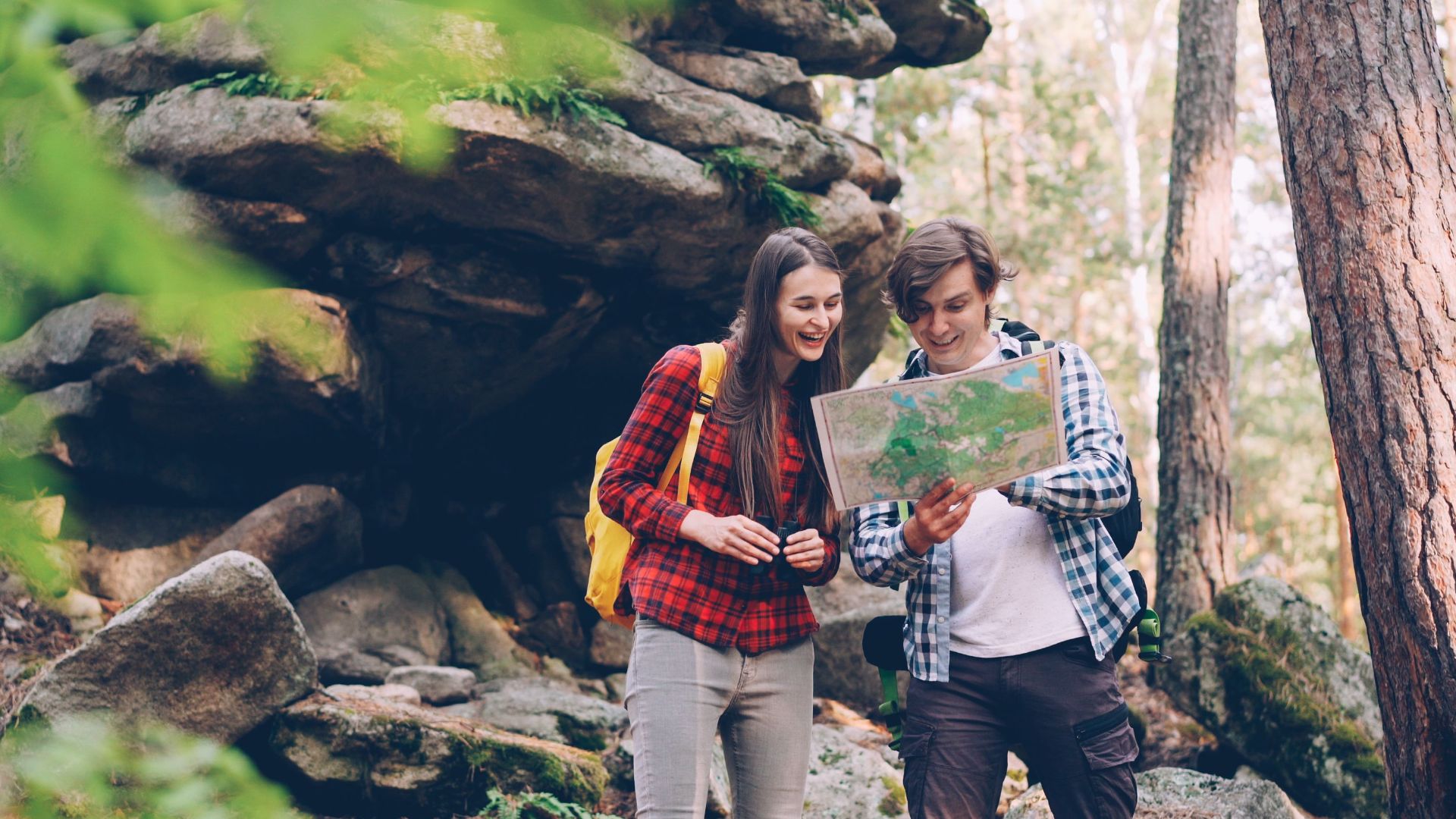 A happy couple in a forest using a map to navigate during their outdoor adventure.