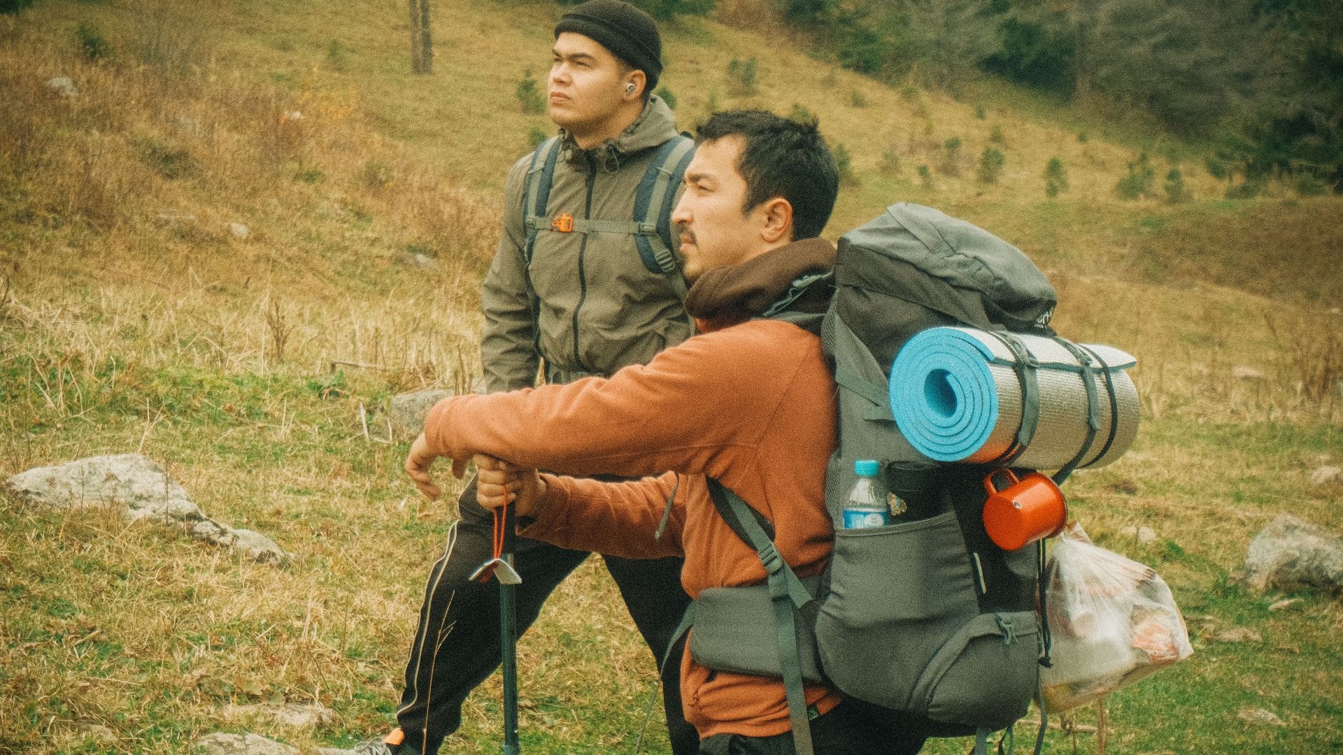 Two hikers with backpacks explore a scenic mountain trail on a foggy day, embracing the adventure.