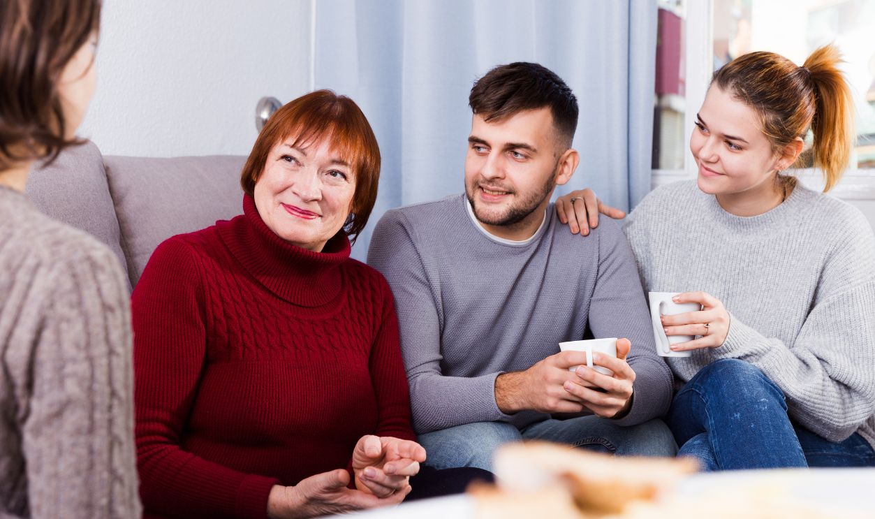 Smiling mature lady with adult children enjoying conversation with female friend at home