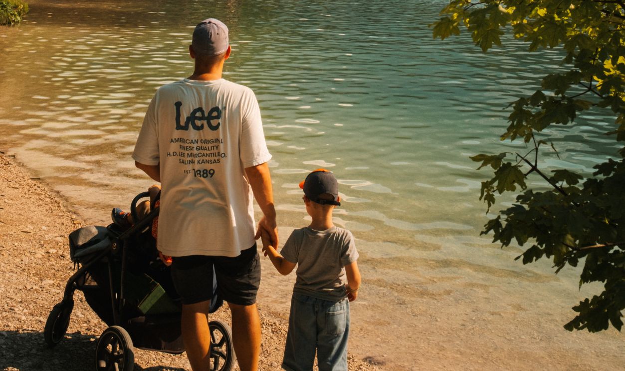 A father and child at a picturesque alpine lake with mountains in the background, surrounded by lush forests