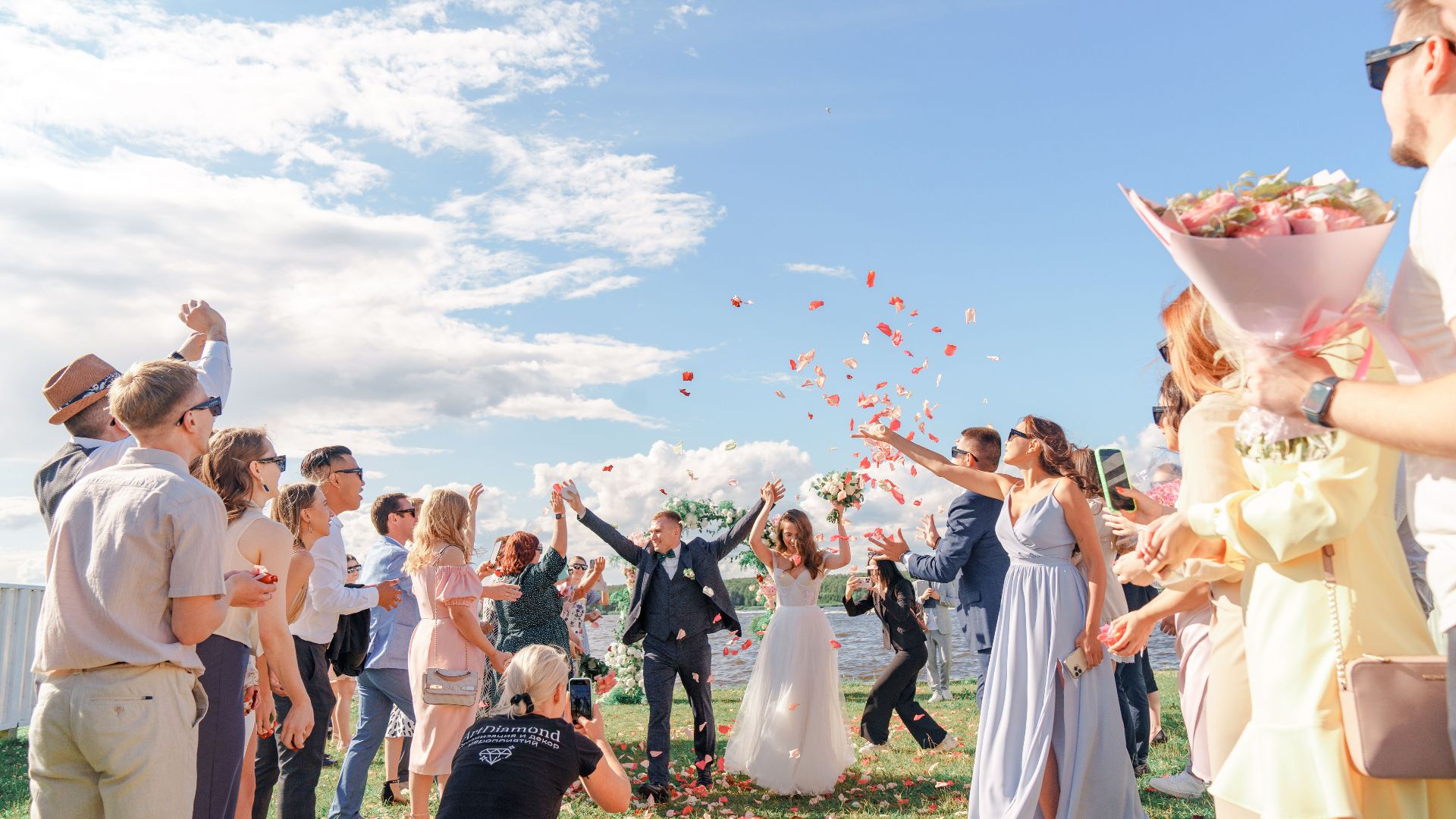 A joyful outdoor wedding celebration with a bride and groom surrounded by guests and confetti.
