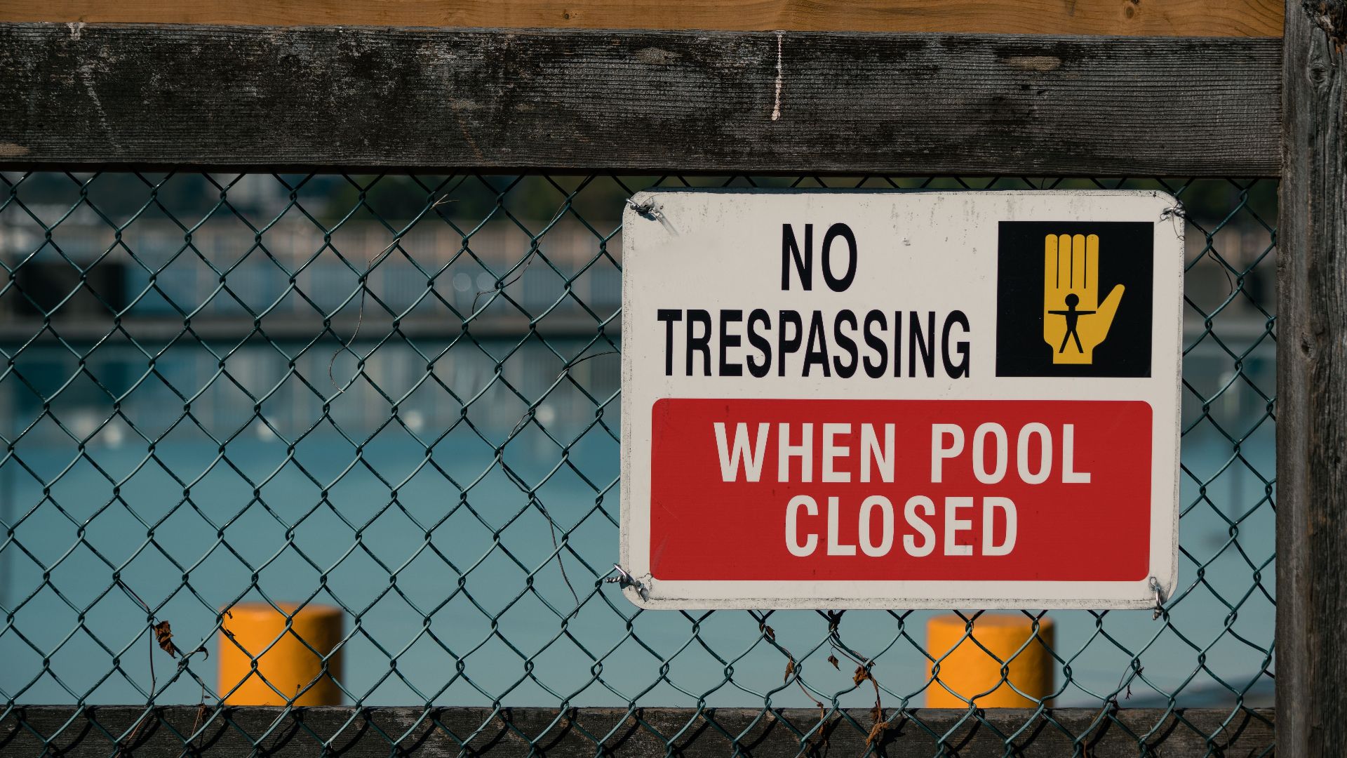 A 'No Trespassing' sign on a chain link fence at a closed swimming pool, ensuring safety and security.