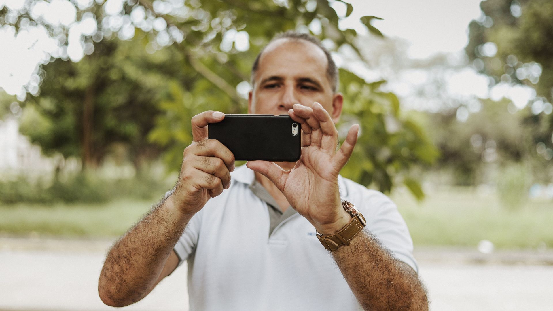 Adult man using smartphone to take a photo in a natural setting, showcasing modern technology and leisure.