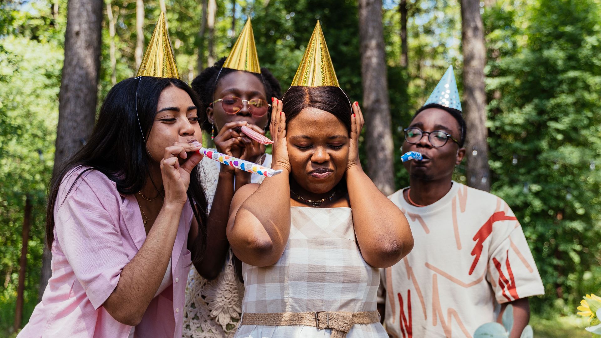 Friends enjoying an outdoor birthday party with party hats and noise makers.