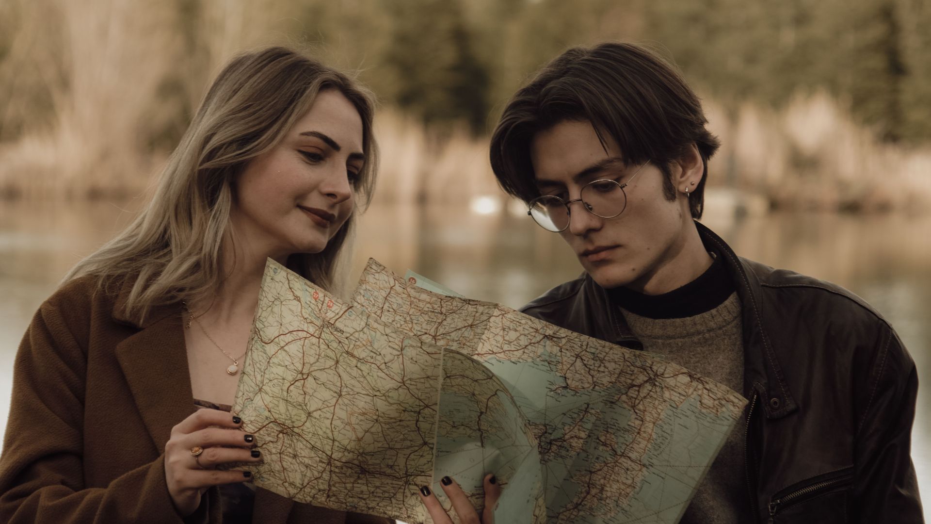 Young couple analyzing a map by a serene lake, planning their travel route in a tranquil nature setting.