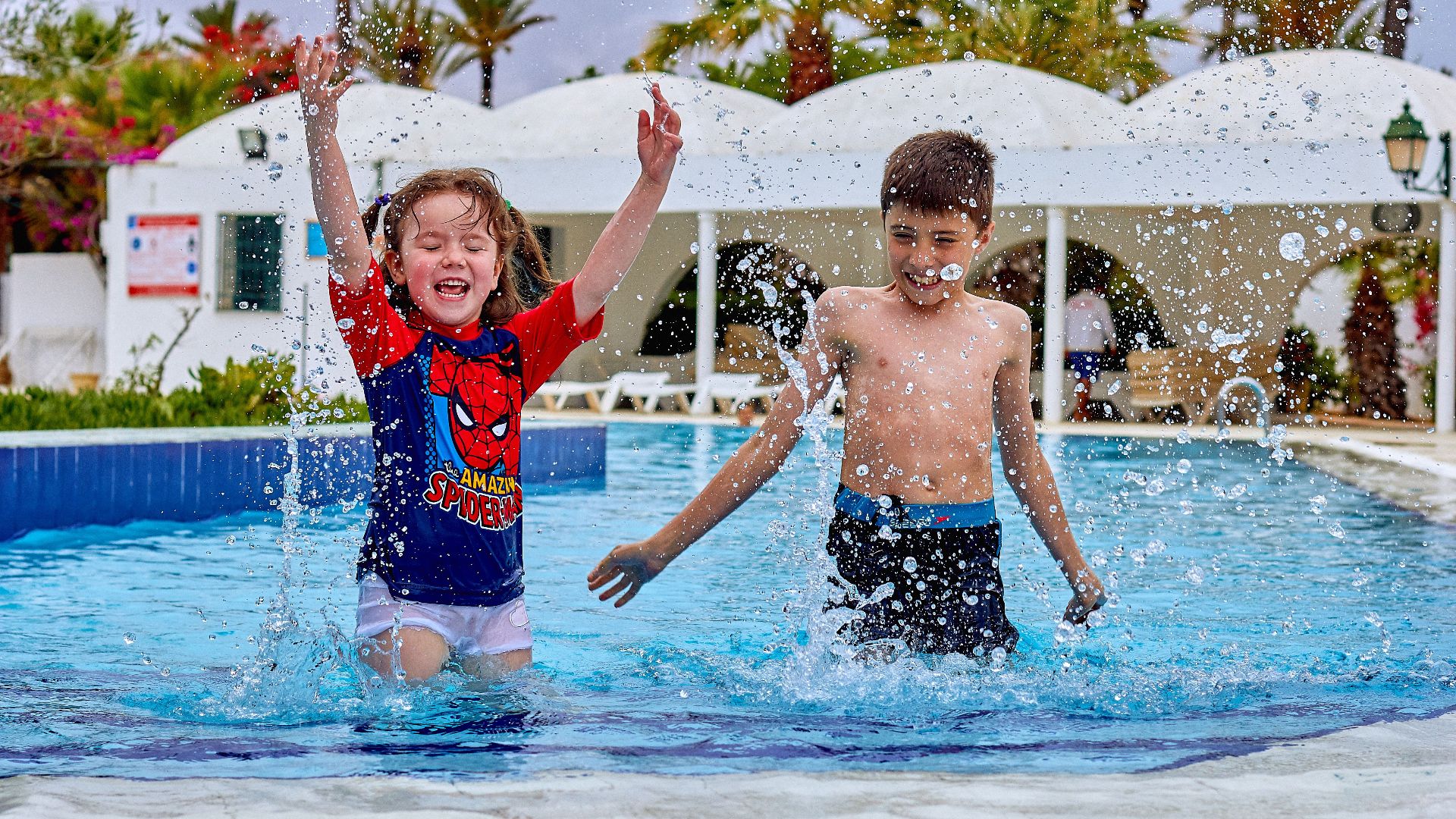 Two kids enjoying a fun day playing and splashing in an outdoor swimming pool.