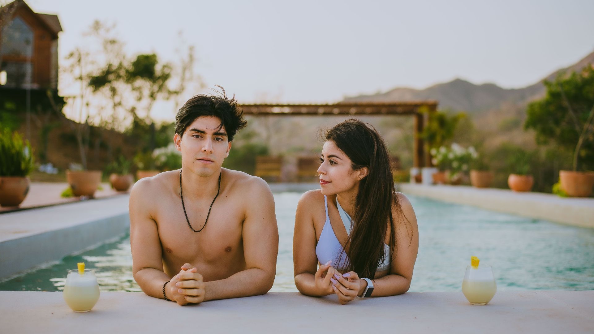 A couple enjoying a relaxing day by the pool in a summer resort setting, surrounded by nature.
