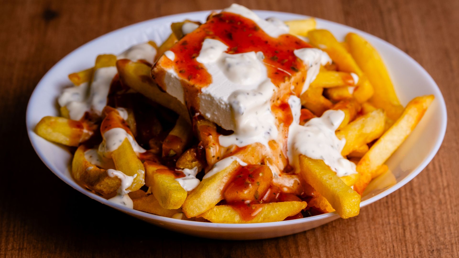 A tempting plate of golden fries topped with rich cheese and vibrant sauces, perfect for a tasty indulgence.