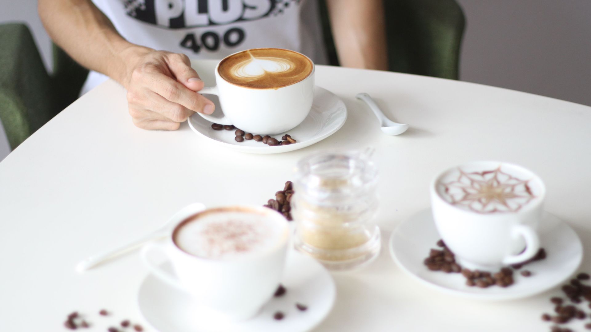 A stylish arrangement of various coffee cups on a café table with a person reaching for one.