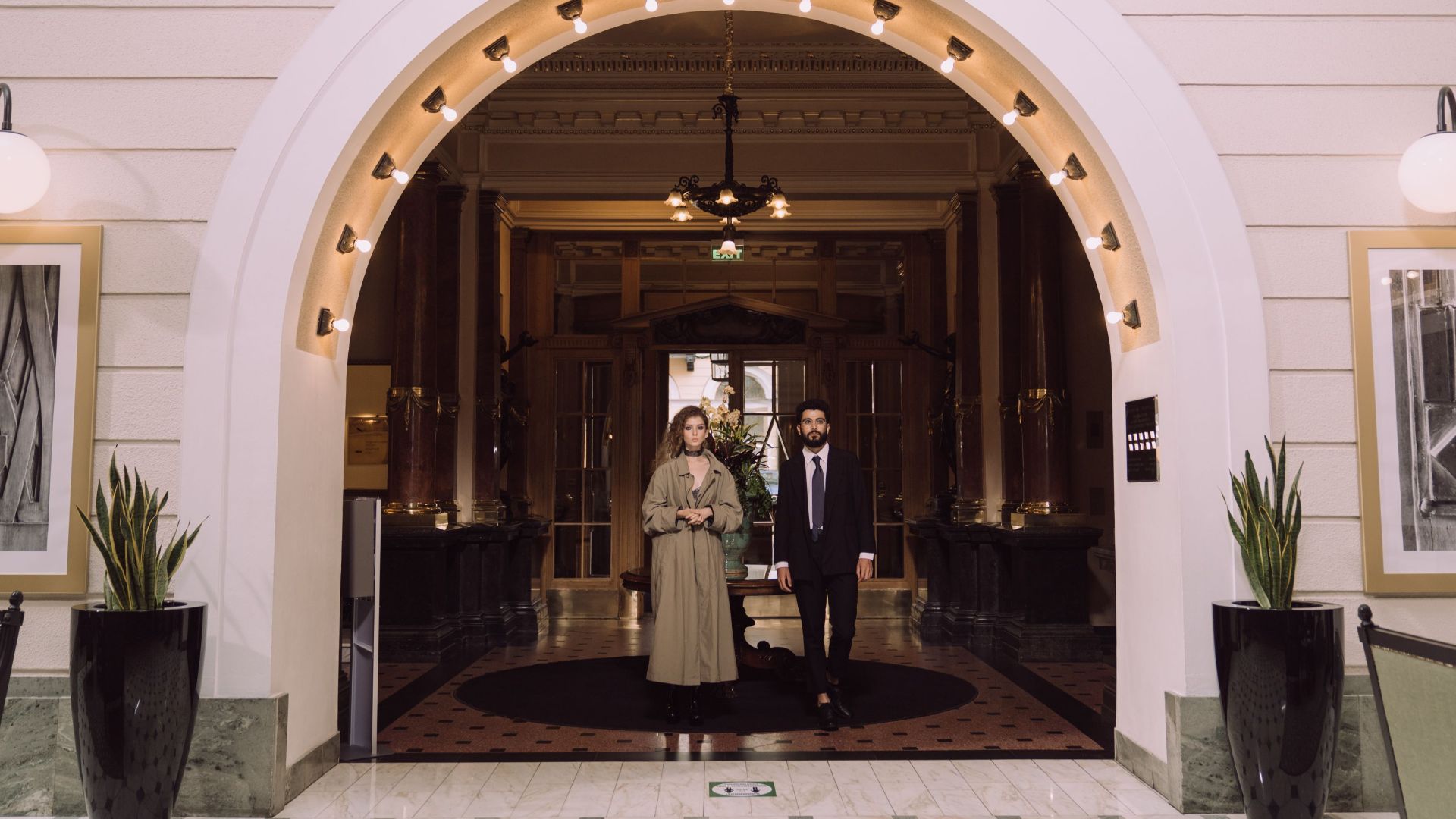 A couple stands at an elegant hotel entrance under a lighted archway.