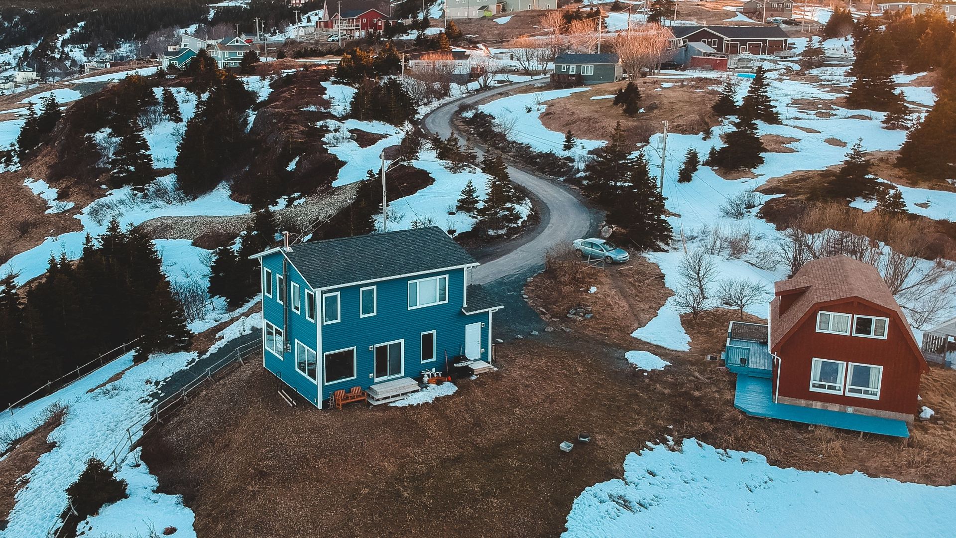 Picturesque drone view of village terrain with colorful houses and conifers covered with snow