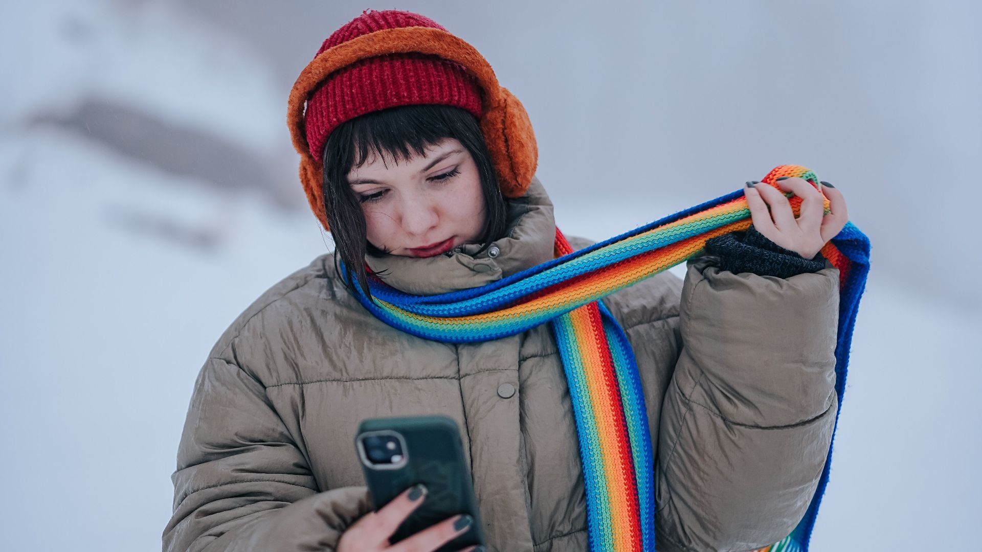 Woman in winter gear checks her phone, surrounded by snow and fog.
