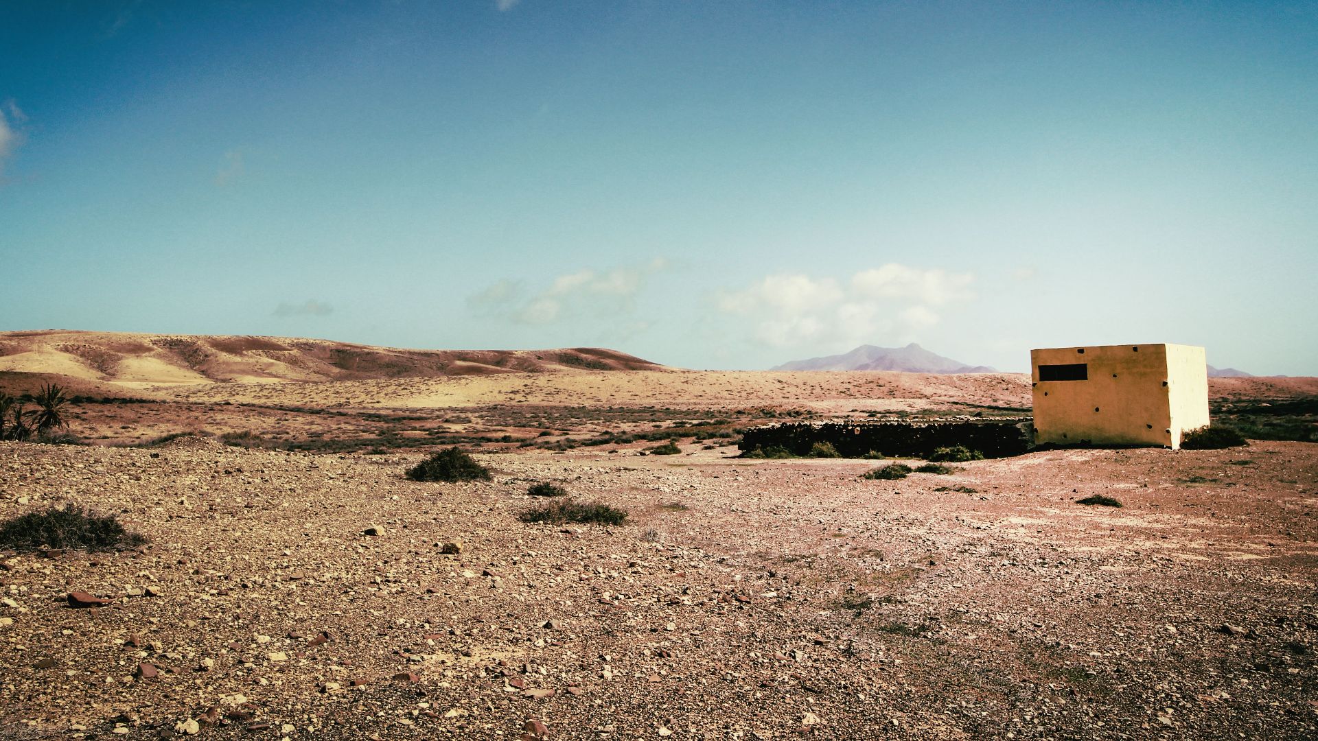 A solitary concrete bunker stands isolated in a barren desert landscape under a clear sky.