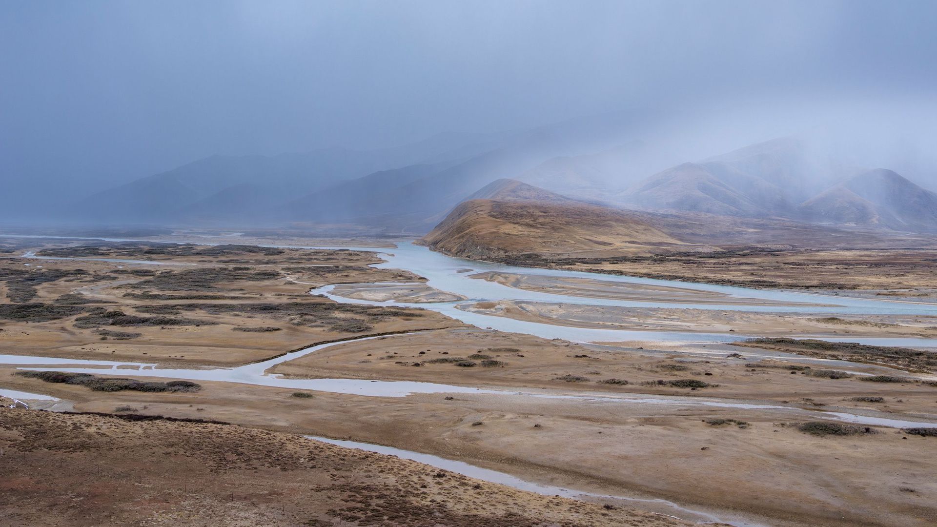Moody landscape of a desert valley with rainfall and winding river