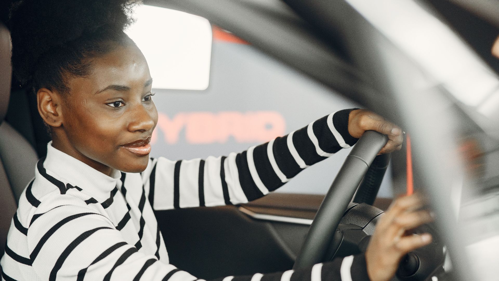 African American woman driving a car, smiling and confident behind the wheel from interior view.