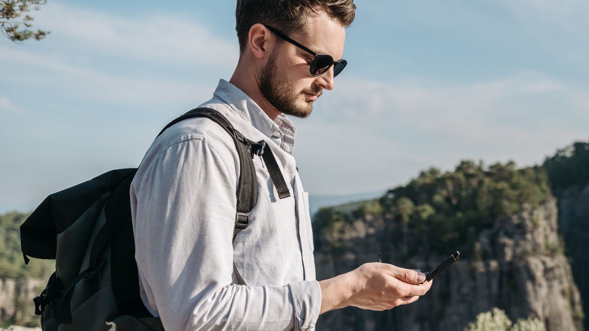 A young man with a backpack enjoys the rugged mountain scenery during a daytime hike.
