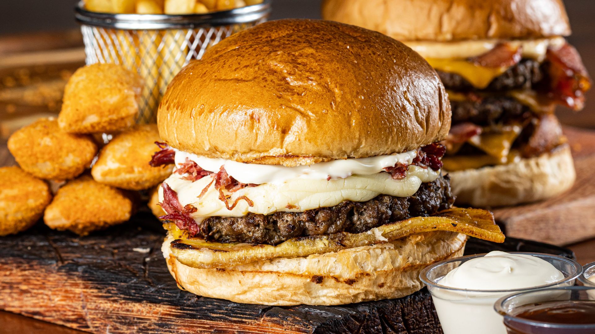 Delicious gourmet burgers with cheese, fries, and dipping sauces on a rustic board.