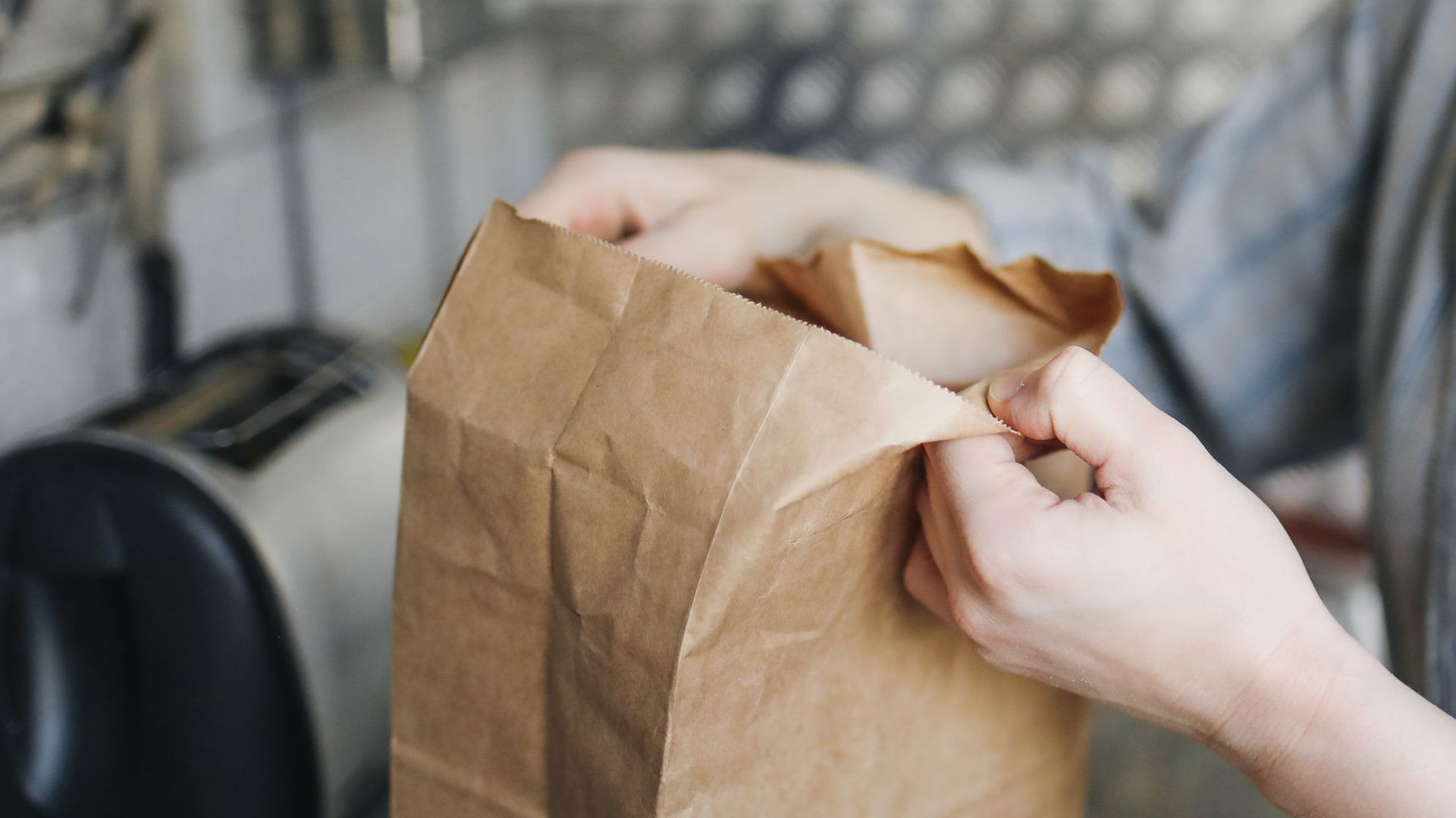 Close-up of a woman opening a paper bag while unpacking groceries in a kitchen setting.