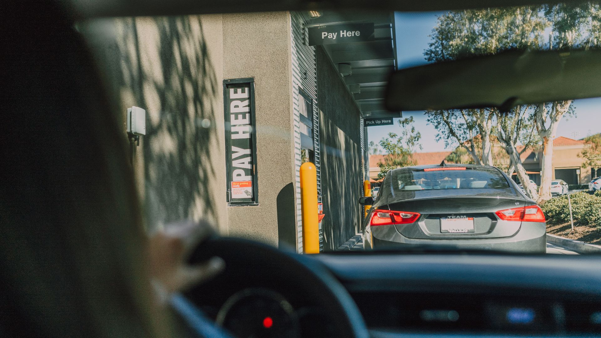 A driver's perspective waiting at a fast food drive-thru queue in daylight.