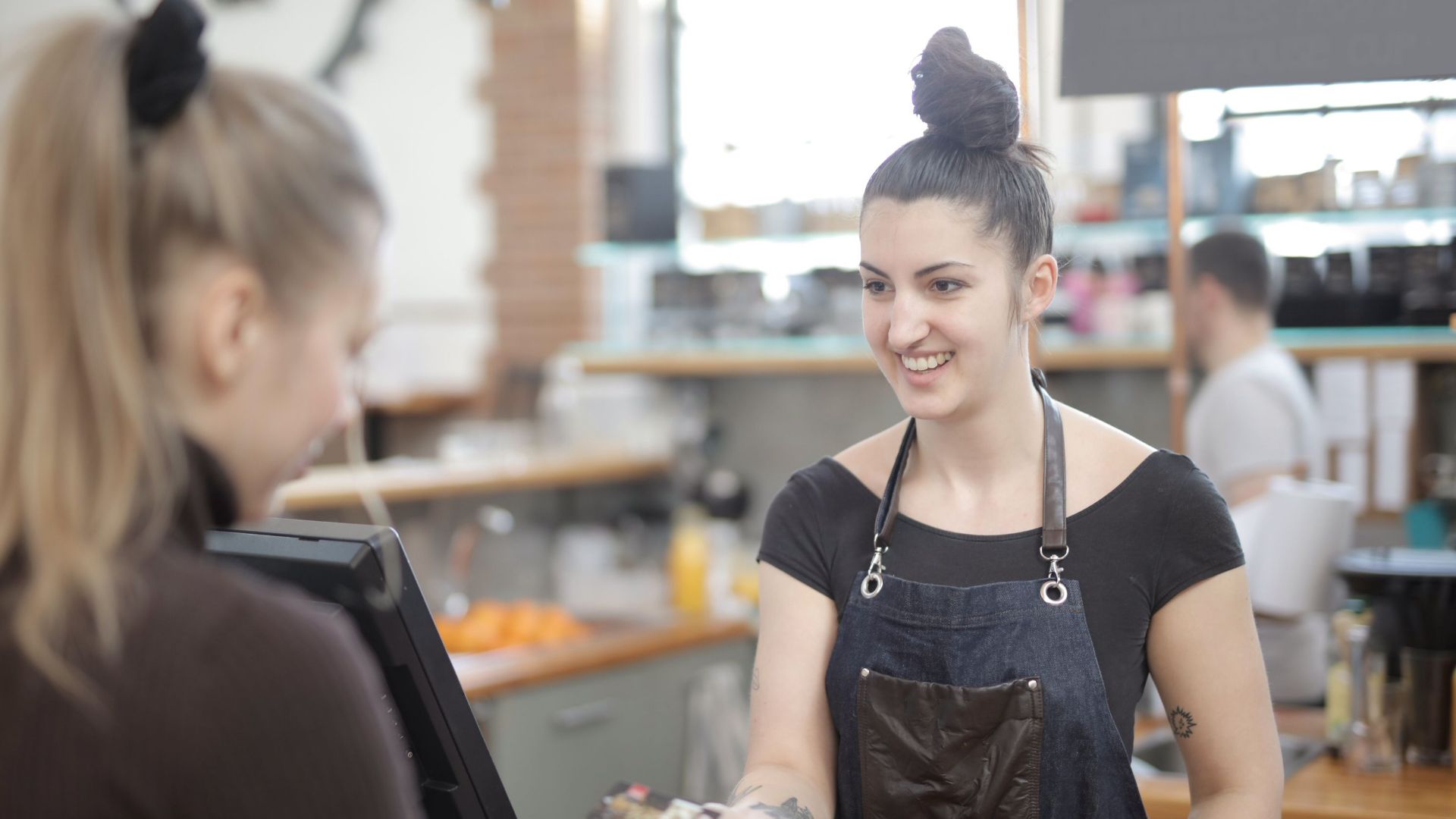 Barista in apron accepting a customer's digital payment in a cozy cafe setting.