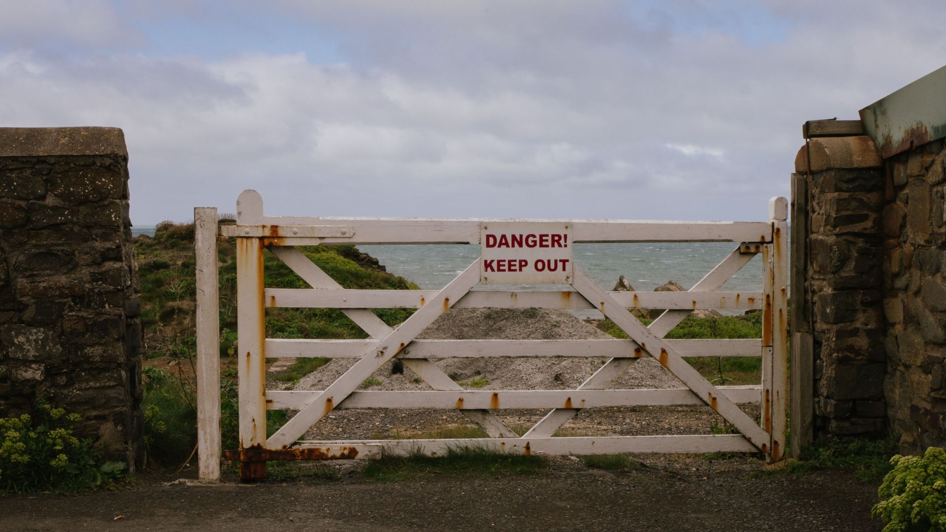 A weathered wooden gate with a danger sign opens to a scenic coastal view.
