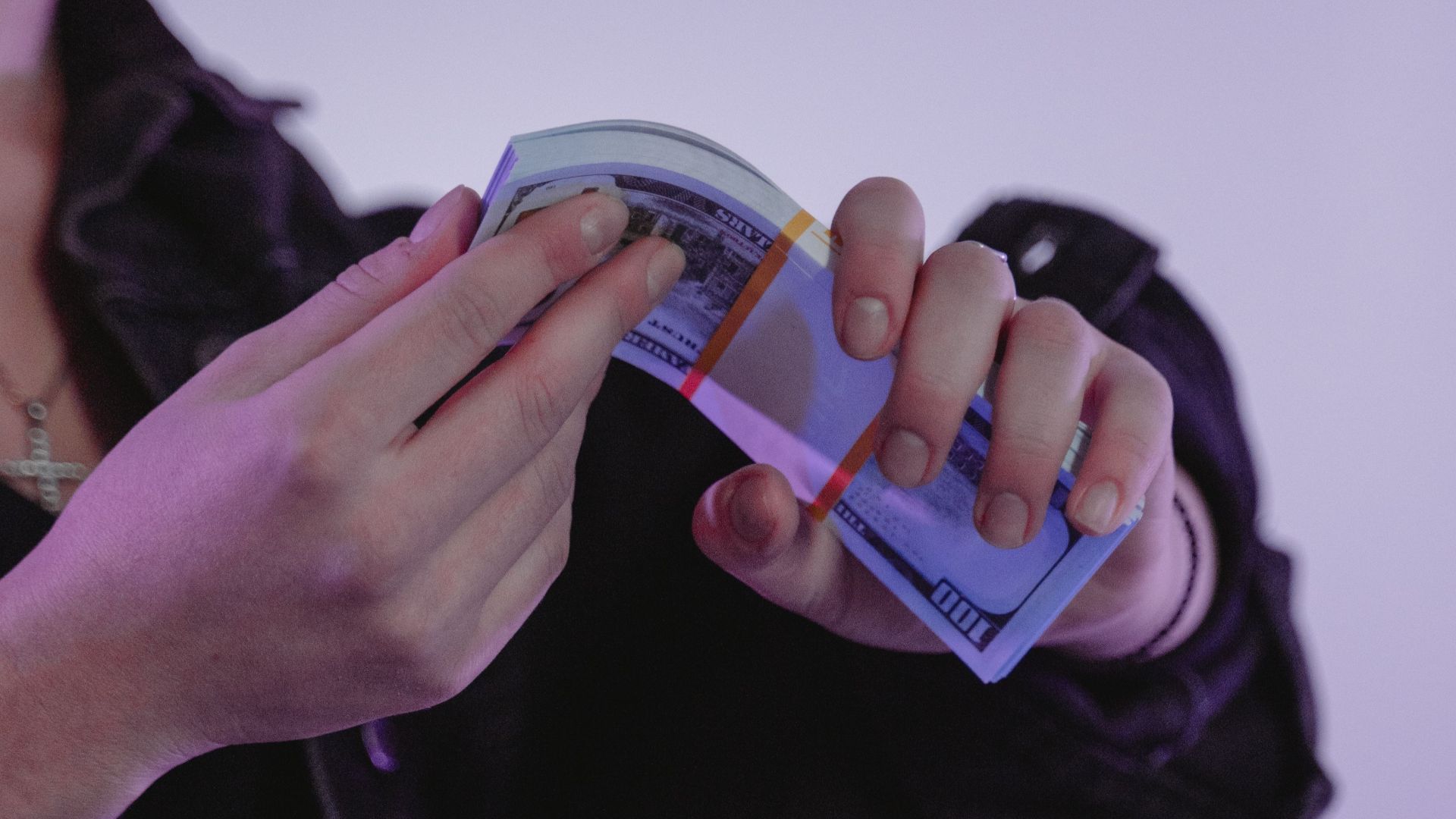 Close-up of a woman counting cash with a purple hue background, wearing a jean jacket.