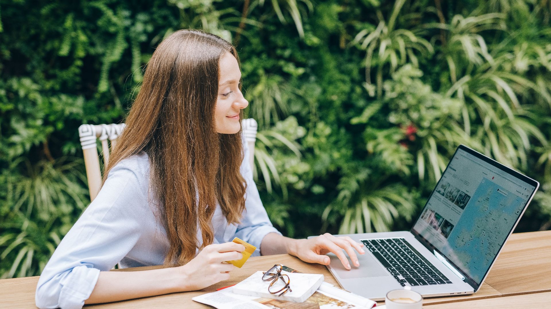 Young woman sitting at a table with a laptop and coffee, enjoying outdoor workspace.