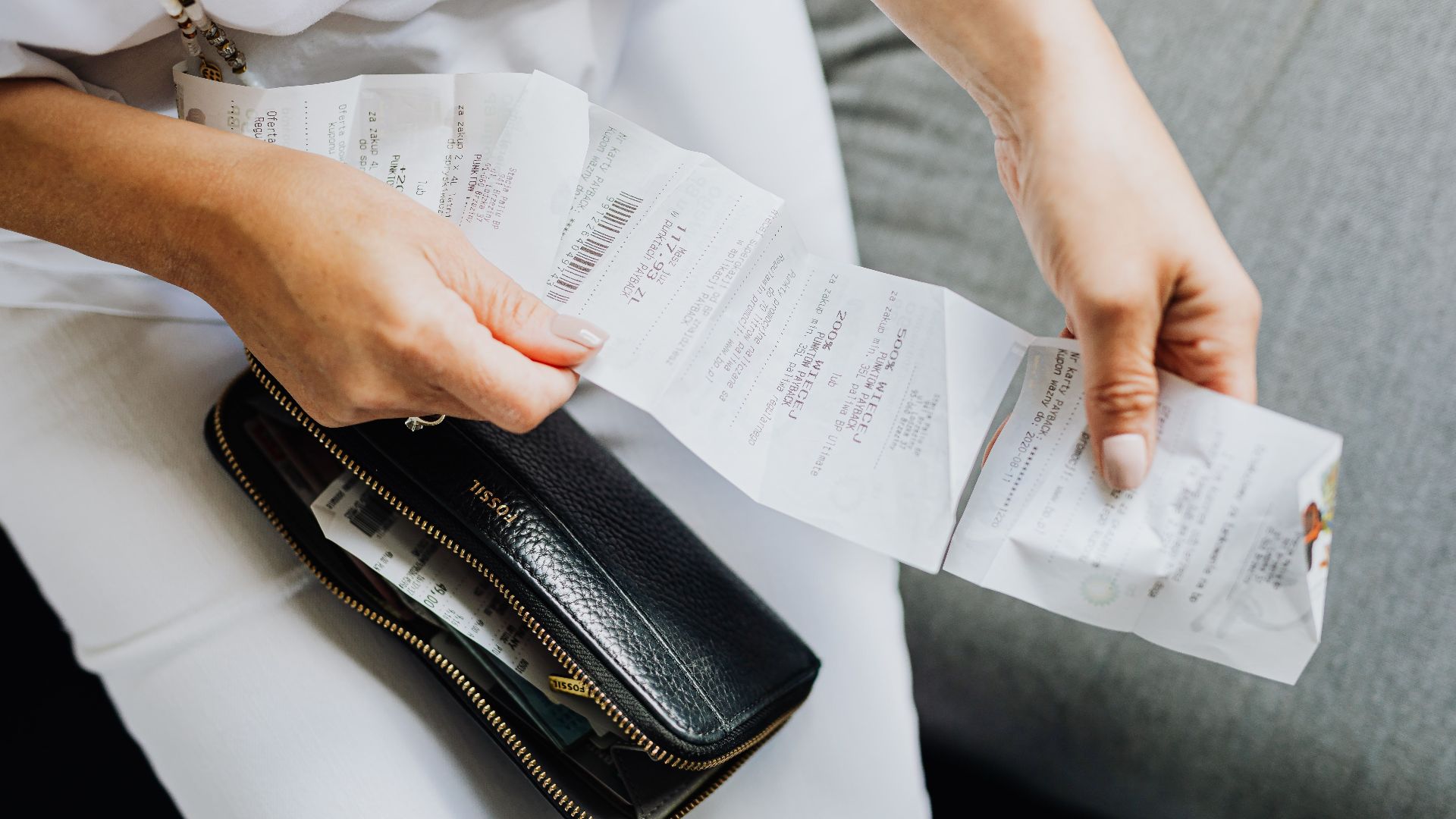 Close-up of a woman's hands managing multiple receipts taken from a black wallet.