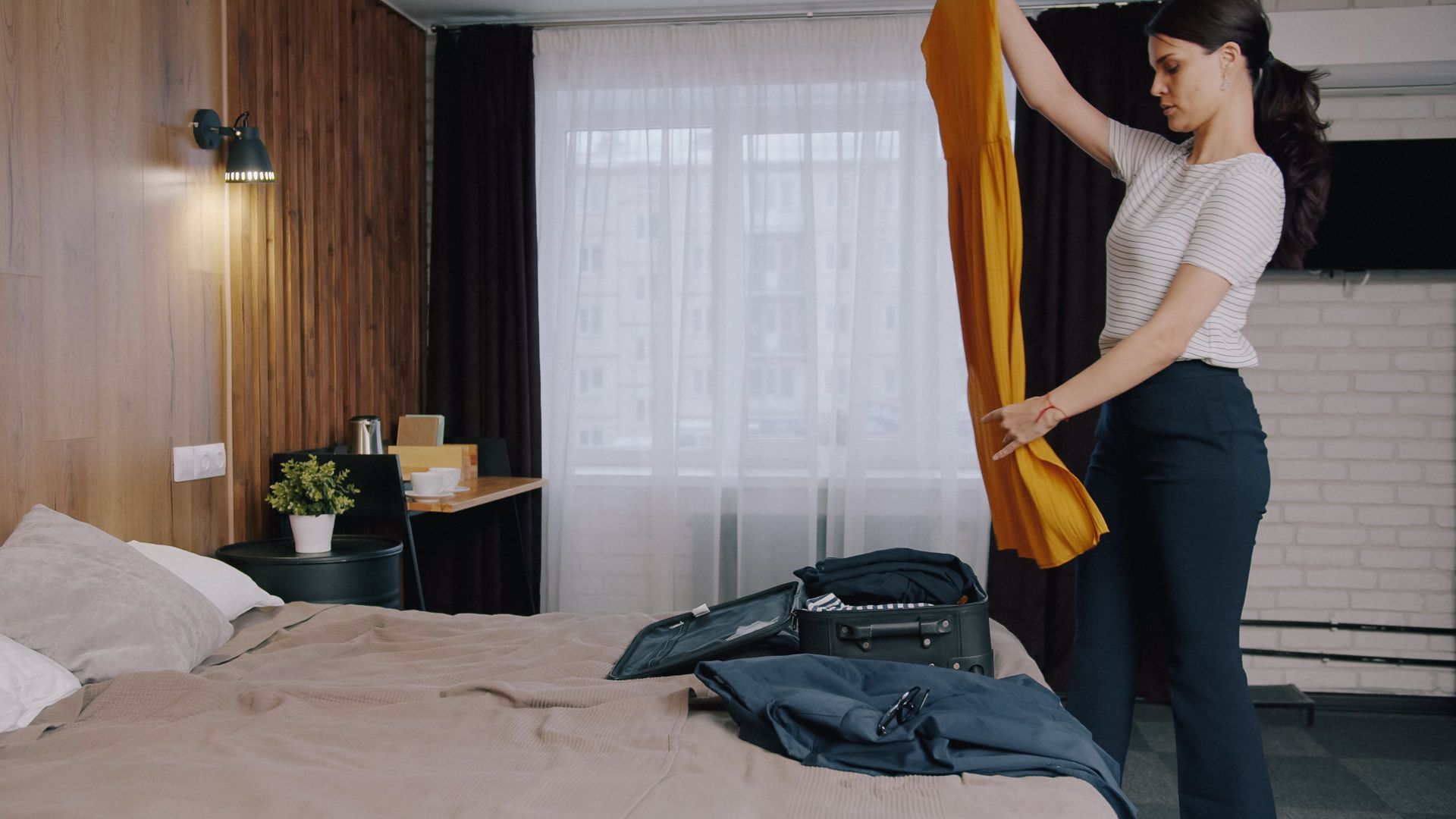 A woman folding clothes while packing in a cozy hotel room with a modern decor.