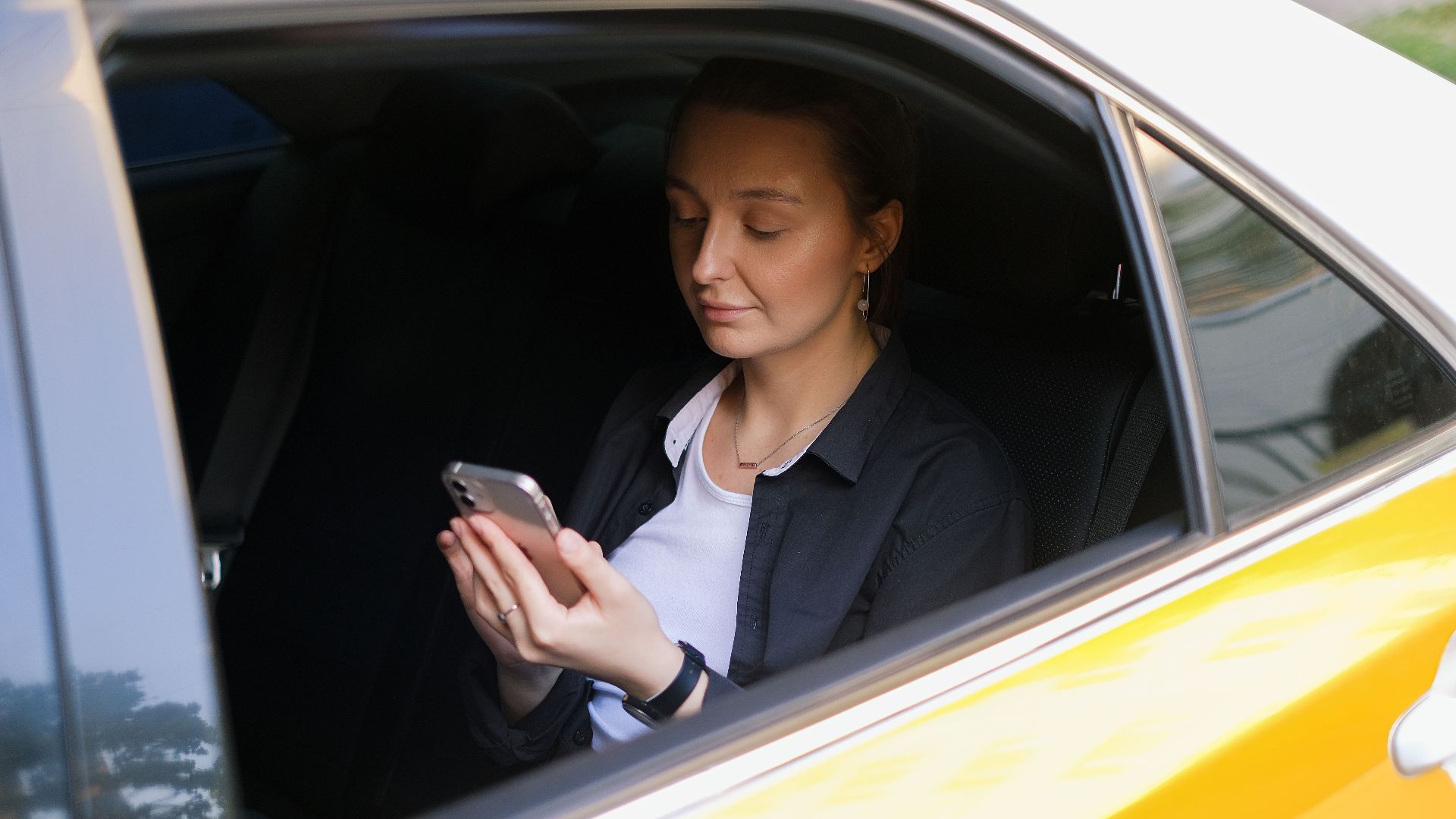 A woman in a taxi, engaged with her smartphone, symbolizing modern remote work culture.