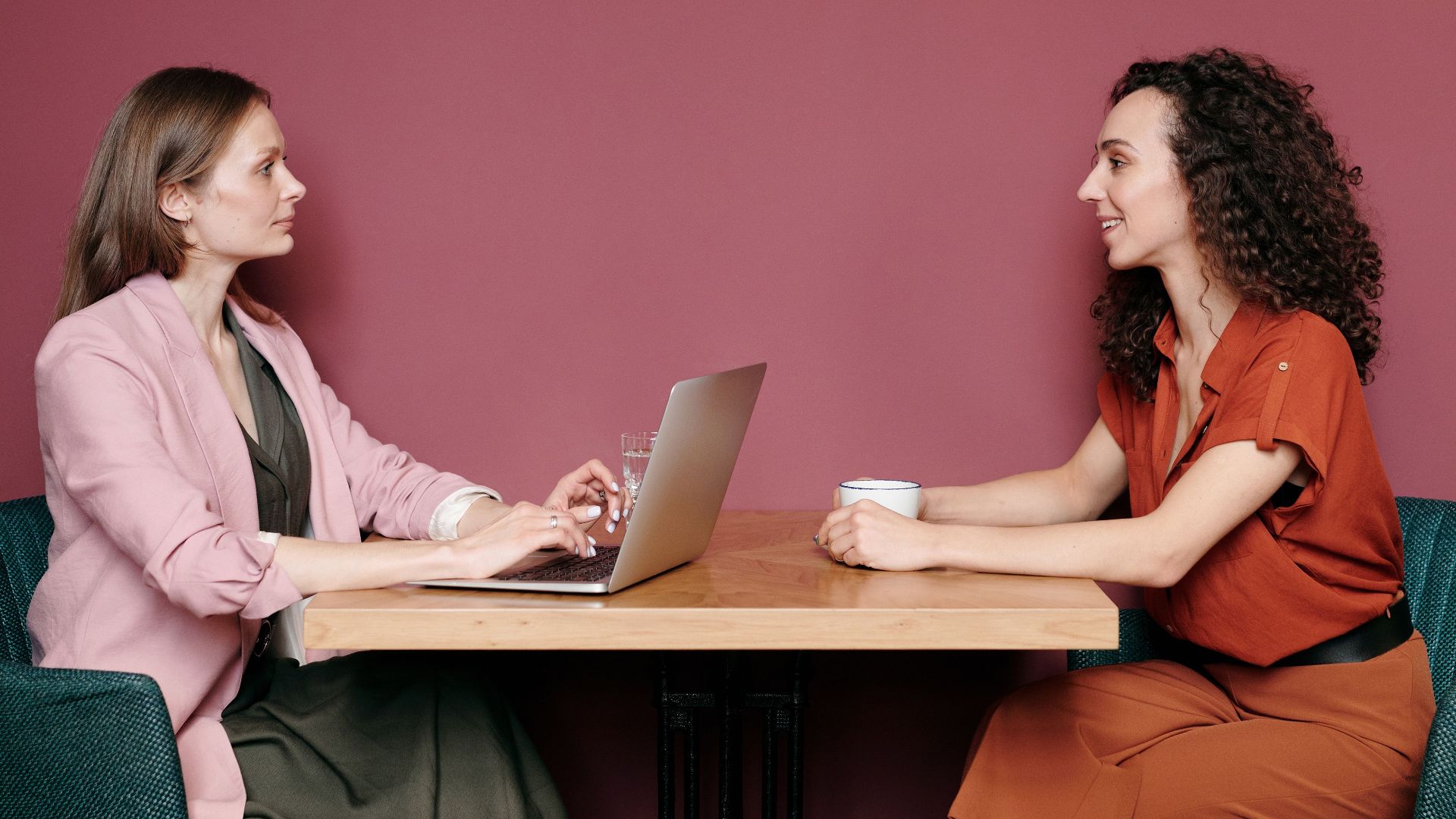 Two women having a meeting at a table with a laptop and coffee inside a stylish room.