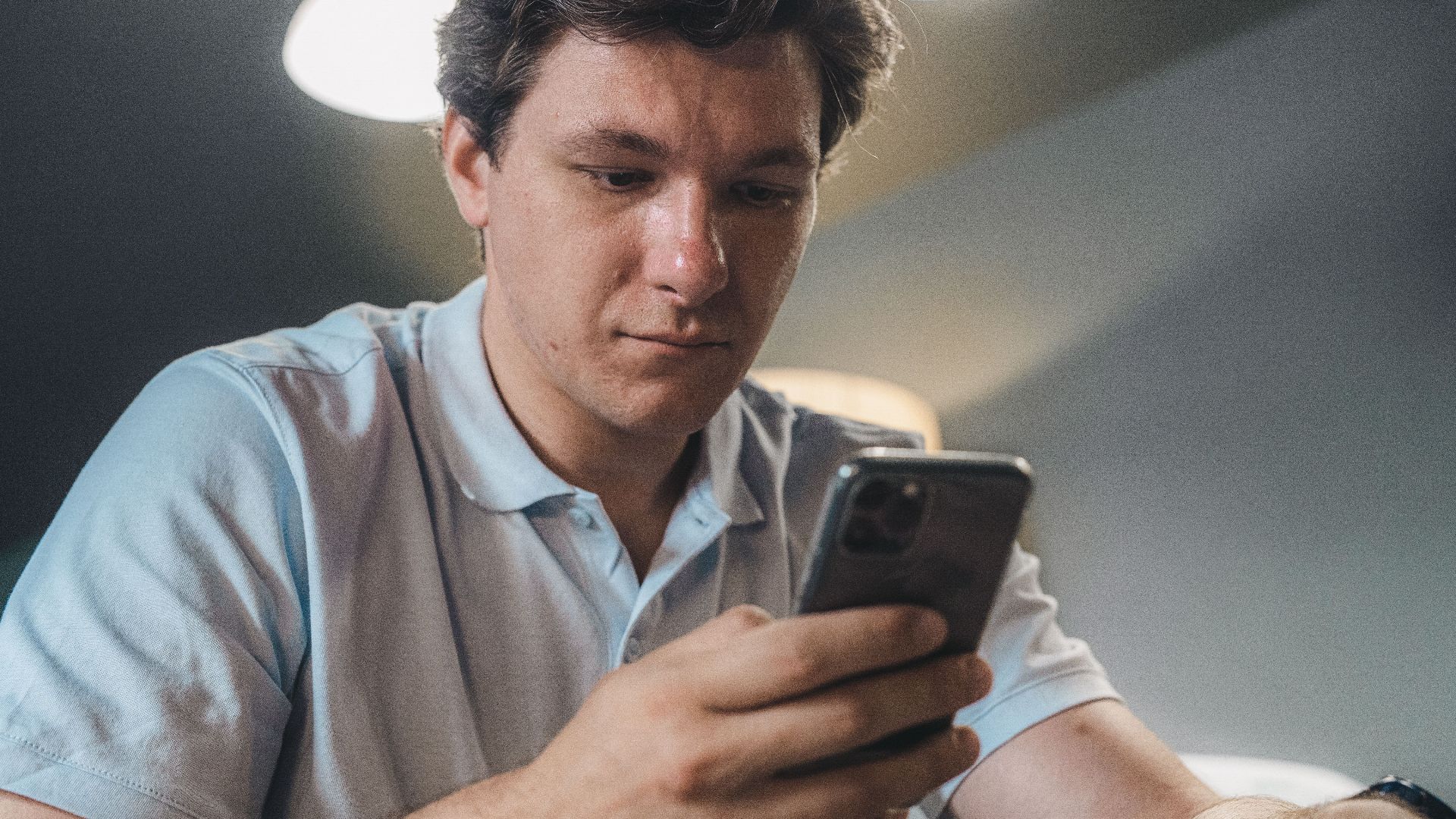 Adult man in casual attire intently using a smartphone indoors, focused and engaged.