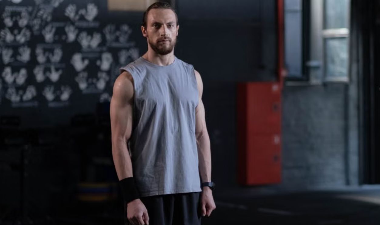 Muscular man standing in a gym with gymnastic rings, showcasing fitness and strength