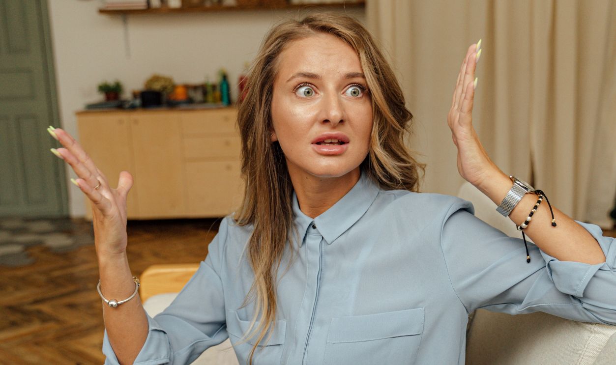 Woman in blue shirt expresses surprise while sitting indoors on a couch