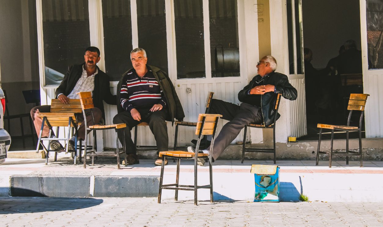 Three elderly men sitting and chatting outside an urban cafe on a sunny day