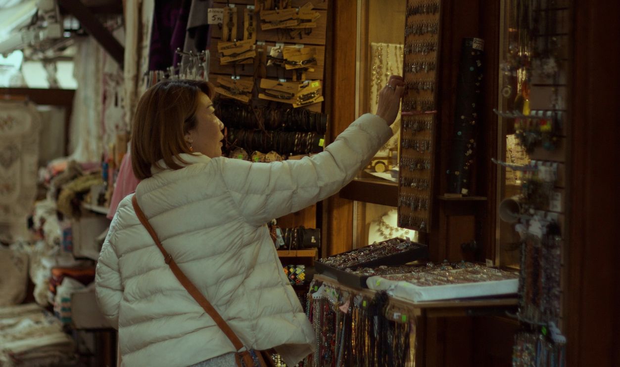 Woman browsing souvenirs at an outdoor market stall, surrounded by various items for sale