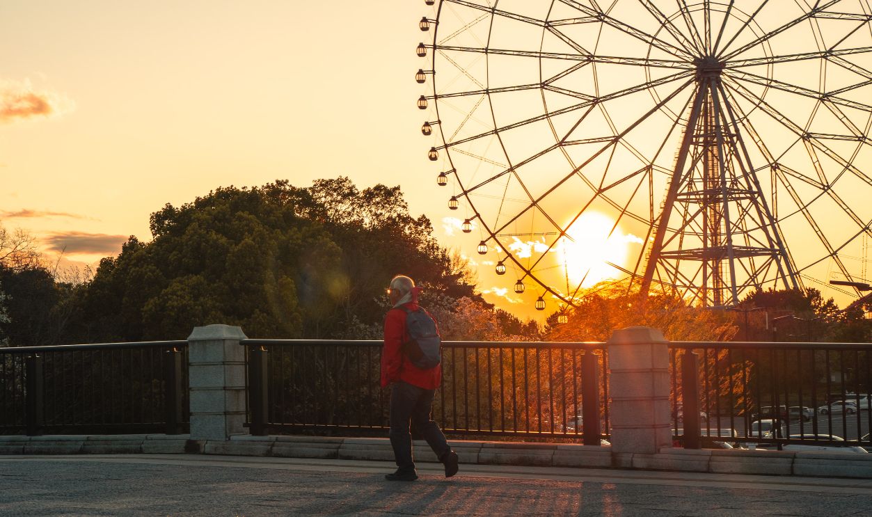 A person walks by a Ferris wheel during a stunning sunset in Tokyo, capturing a warm and serene moment